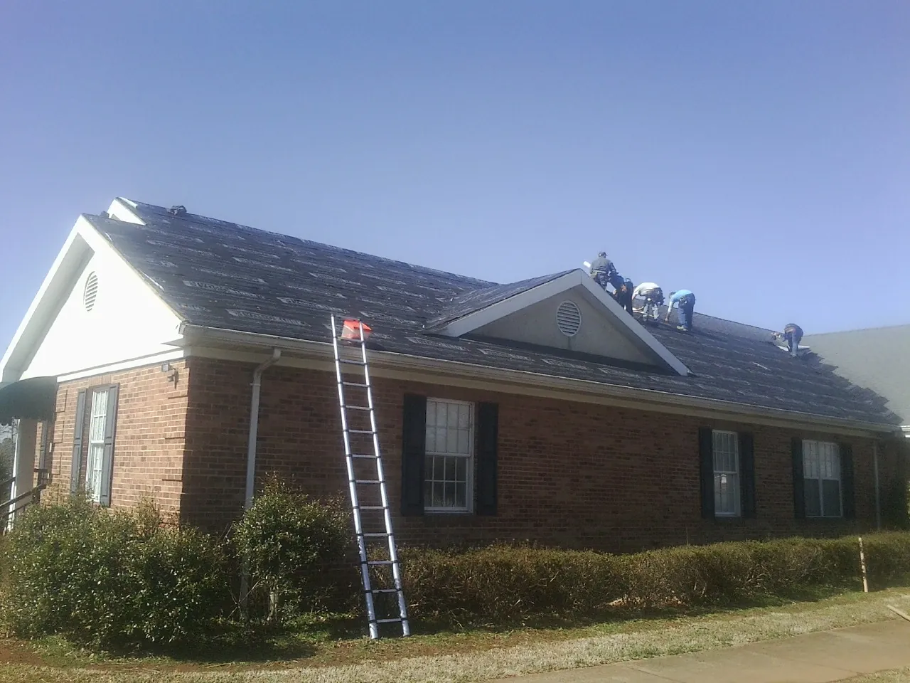 Crew tearing shingles off a brick ranch roof with a ladder set — Emergency Roof Repair work by our crew in West Springfield