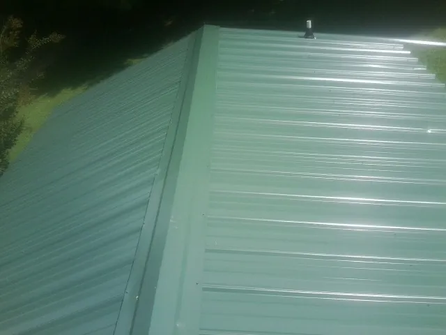 New green metal panels meeting at the ridge of a roof — Flat Roof Repair work by our crew in West Springfield