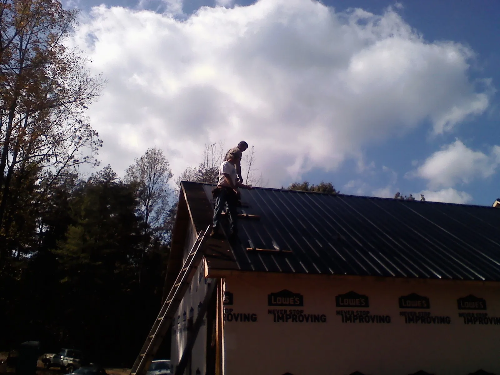 Roofer fastening dark metal panels high against a cloudy sky, from a Roof Inspection job in West Springfield